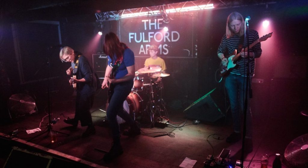 Photograph of four people playing rock music enthusiastically.