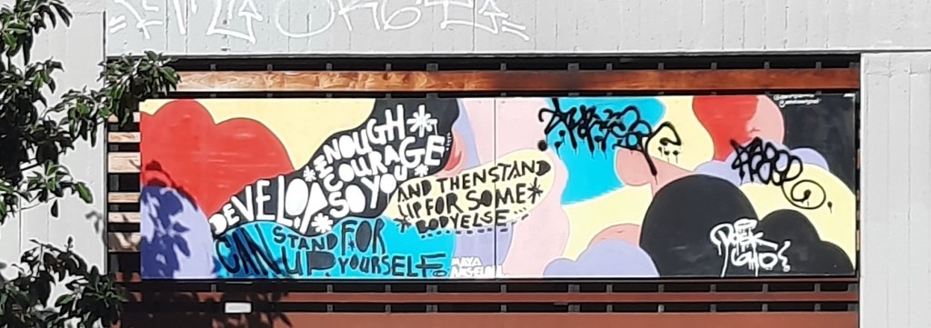 Photo of graffiti against a colourful background. It reads as follows. Develop enough courage so you can stand up for urself and then stand up for somebody else.